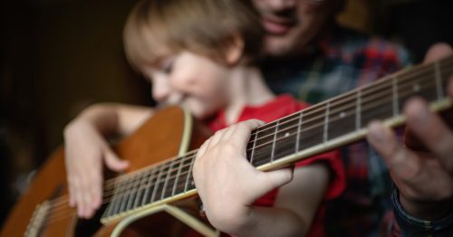 filho Father teaching his little son to play guitar in home