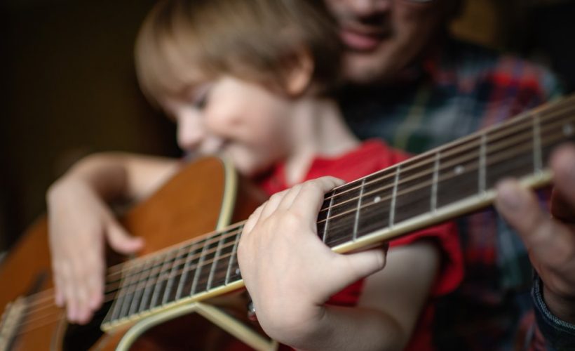 filho Father teaching his little son to play guitar in home